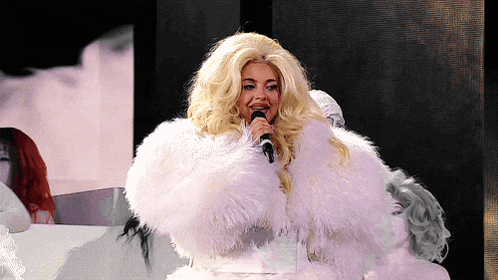 a blonde woman in a white fur coat singing into a microphone