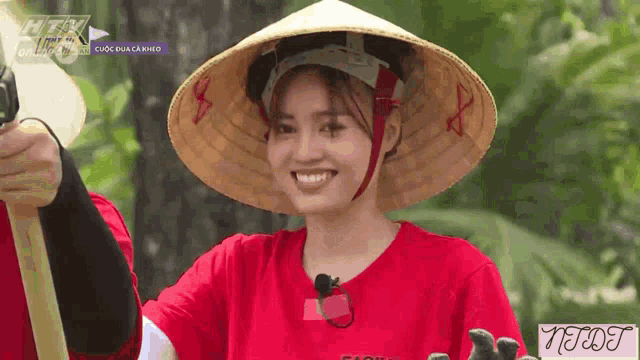 a woman wearing a red shirt and a conical hat is smiling for the camera