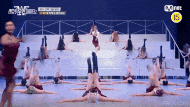 a group of dancers are performing on a stage with a yellow sign that says mnet 15