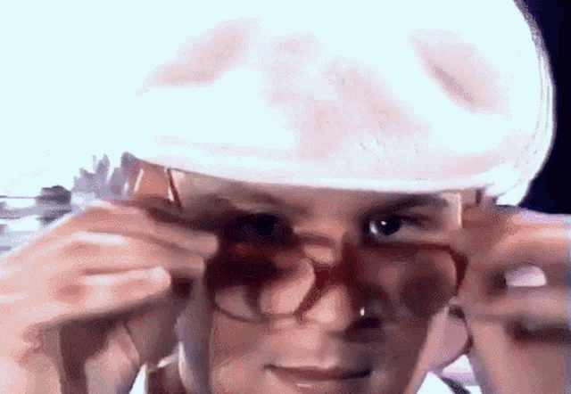 a man wearing glasses and a hat is adjusting his glasses .