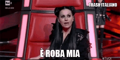 a woman is sitting in a red chair with the words e roba mia written on the screen .