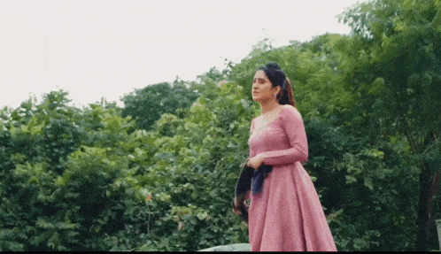 a woman in a pink dress stands in front of a forest