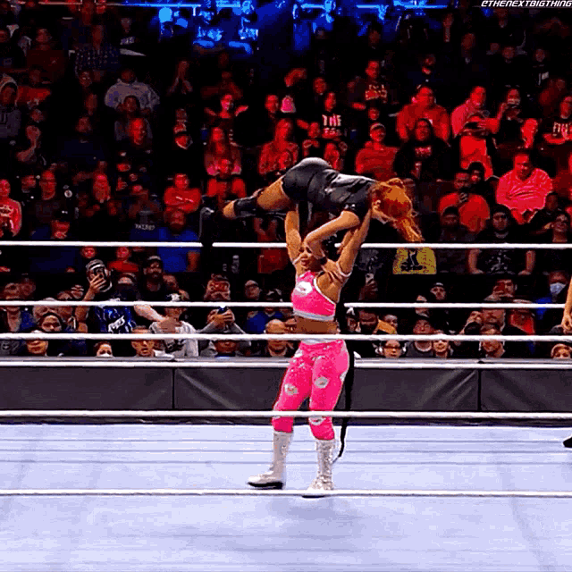 a woman in a pink outfit is being lifted in the air by another woman in a black outfit