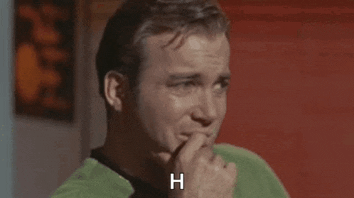 a man in a green shirt is holding his finger to his chin and says `` h '' .