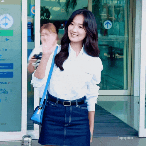 a woman wearing a white shirt and a blue skirt stands in front of a delta airlines building