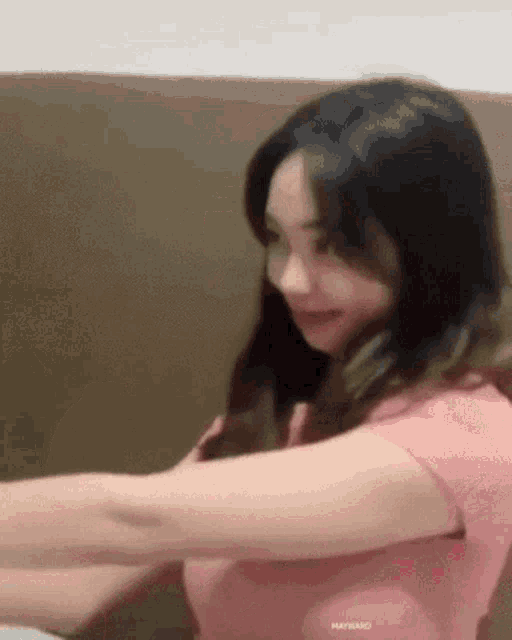 a woman in a pink shirt is sitting on a couch and smiling .