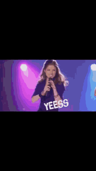 a woman singing into a microphone on a stage with the word yeess written on it