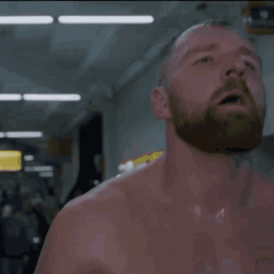 a shirtless man with a beard is sweating while standing in a gym .
