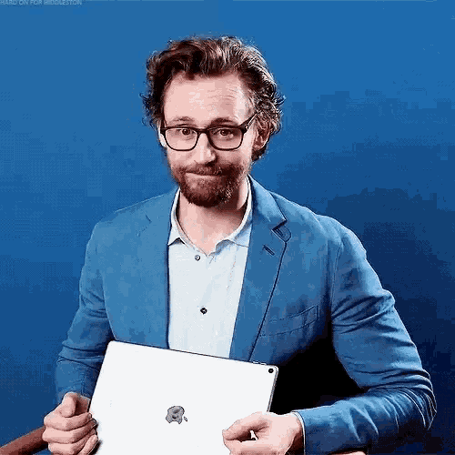 a man wearing glasses and a blue jacket is holding a tablet computer .