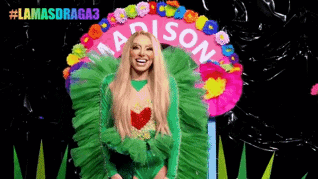 a woman in a green dress is standing in front of a sign with flowers on it .