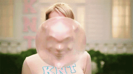 a woman is blowing a giant bubble gum balloon in front of her face .