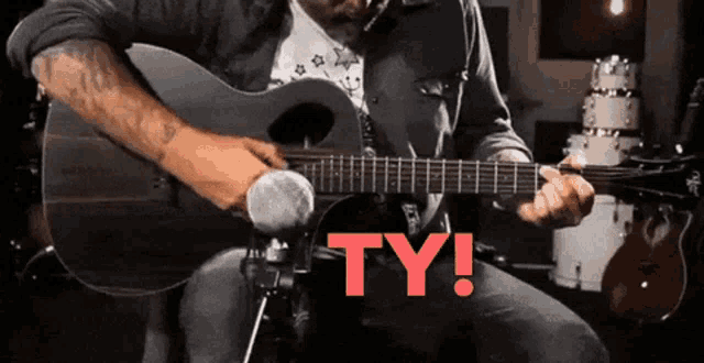 a man playing an acoustic guitar with the word ty in red behind him