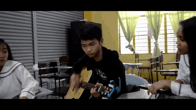 a boy playing an acoustic guitar in a classroom with other students
