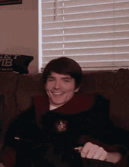 a man is smiling while sitting on a couch next to a window