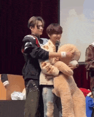 a man is holding a teddy bear while standing next to another man on a stage .