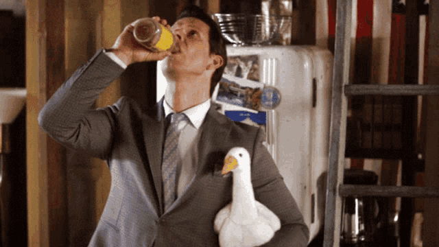 a man in a suit drinking from a bottle while holding a stuffed duck