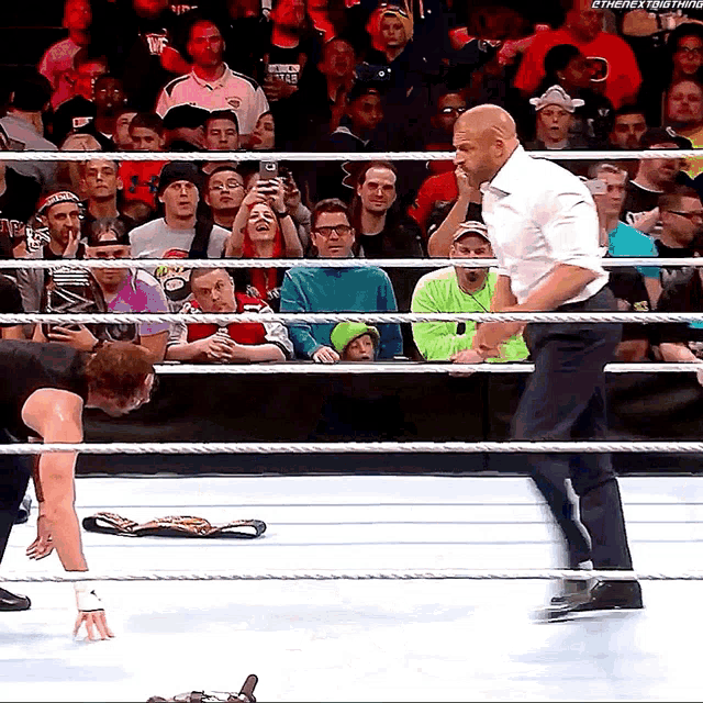 a man in a white shirt stands in a wrestling ring with a crowd watching