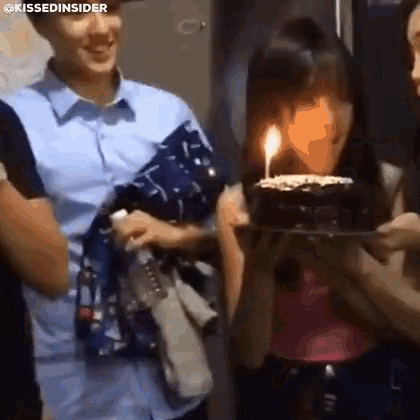 a woman is holding a cake with a lit candle in front of her face .