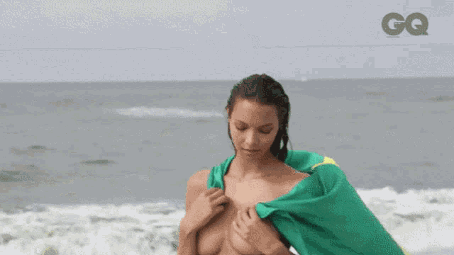 a naked woman is holding a brazilian flag on the beach .