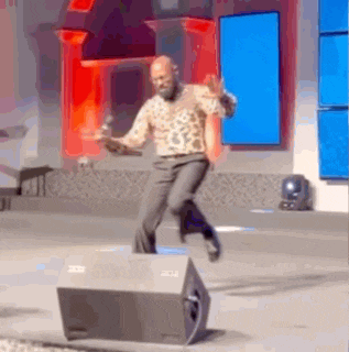 a man in a leopard print shirt is dancing on a stage in front of a speaker .