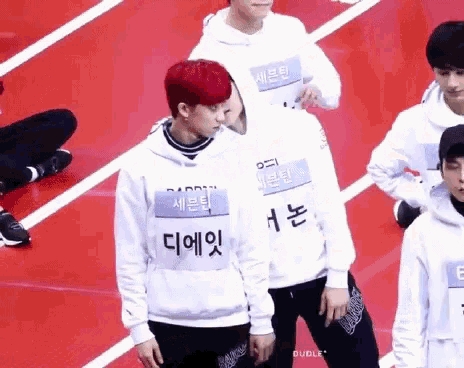 a group of young men are standing on a red track wearing white sweatshirts .