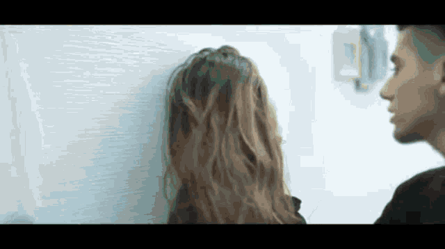 a woman is leaning against a wall while a man looks on .