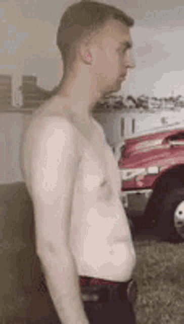 a shirtless man standing in front of a red truck .