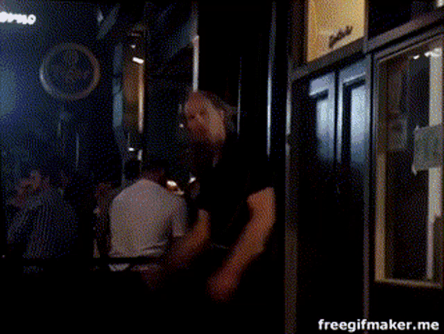 a man in a black shirt is dancing in a dark room with a freegifmaker.me watermark