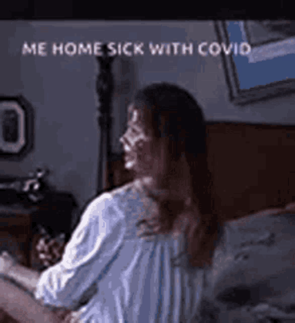 a woman is sitting on a bed with the words `` me home sick with covid '' written on her face .