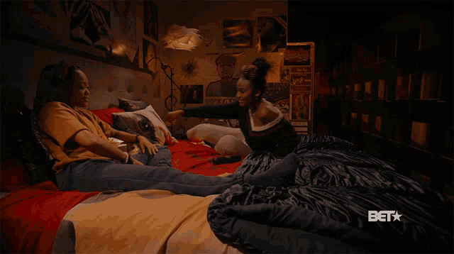 two women sit on a bed with a bet logo on the bottom
