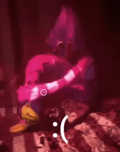 a pink cartoon character is sitting on a bed with a sad face on his face .
