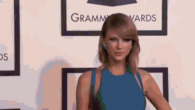 taylor swift is wearing a blue dress and standing on a red carpet at the grammy awards .