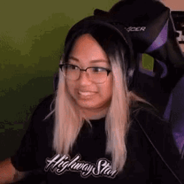 a woman wearing glasses and headphones is smiling while sitting in a gaming chair .
