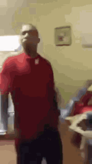 a man in a red shirt is standing in a room with his hands on his hips .