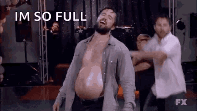 a man with a very large belly is dancing on a stage with other people .