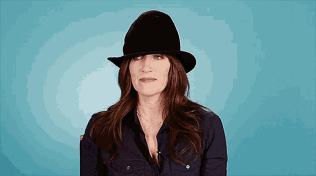 a woman wearing a black hat and a black shirt against a blue background