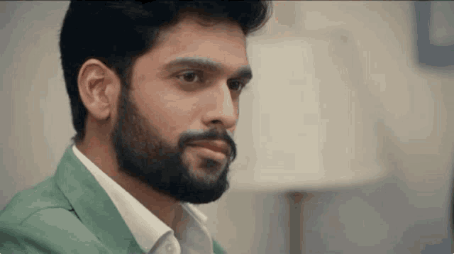 a man with a beard is wearing a green jacket and a white shirt