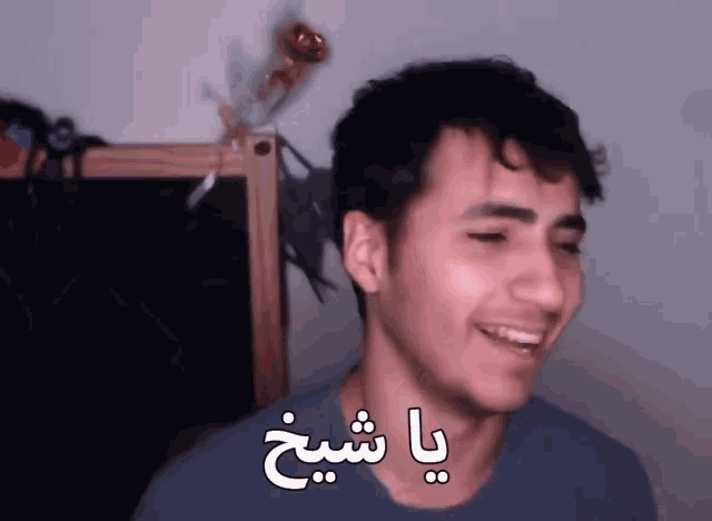 a man with arabic writing on his face smiles in front of a blackboard