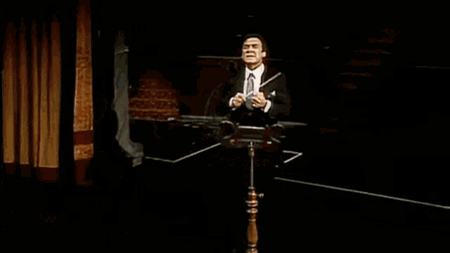 a man in a suit and tie is standing at a podium in the dark holding a baton .