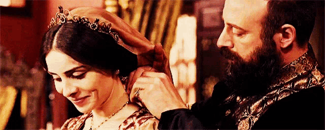 a man with a beard is putting a tiara on a woman 's head .