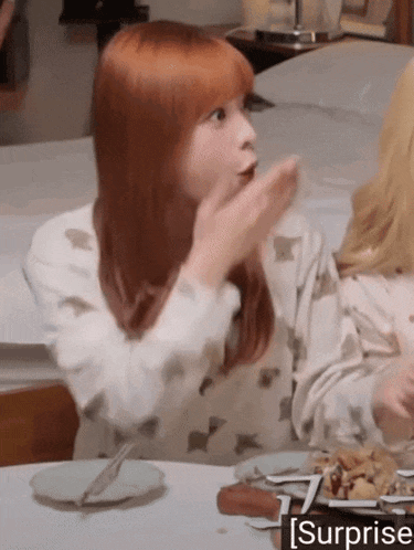 a girl with red hair is sitting at a table with plates of food and a surprise sticker on the bottom