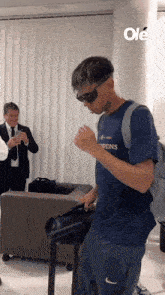 a man wearing sunglasses and a blue shirt is dancing in a room .