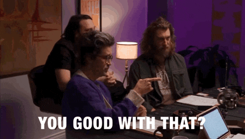 a group of men are sitting around a table and one of them is pointing at another man and says you good with that