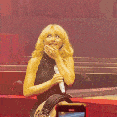 a woman covering her mouth with her hand while holding a microphone on a stage