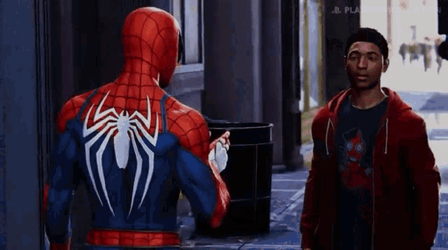 a man in a red hoodie is standing next to a man in a spiderman suit .