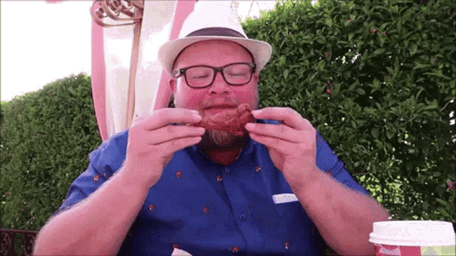 a man in a hat and glasses is eating a piece of chicken