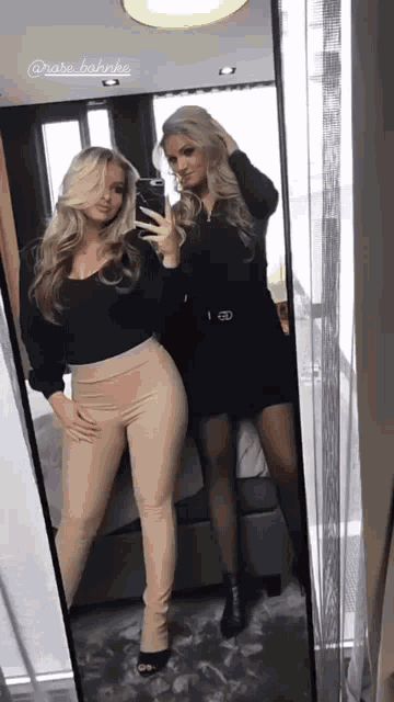 two women are taking a selfie in front of a mirror and one of them is wearing a black shirt