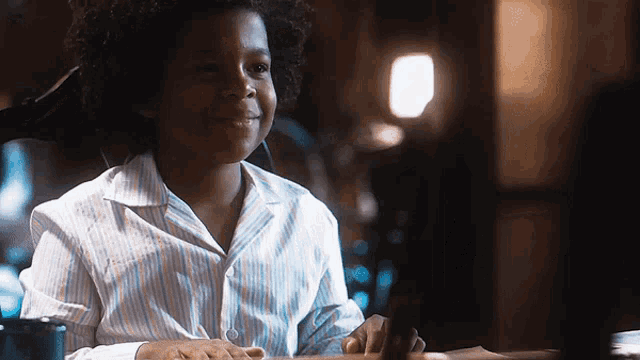 a young boy in a striped shirt is smiling while sitting at a table