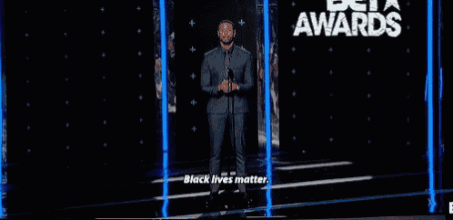 a man in a suit is standing on a stage with a microphone and a sign that says black lives matter .