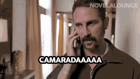 a man with a mustache is talking on a cell phone and the words camaradaaaa are written above him